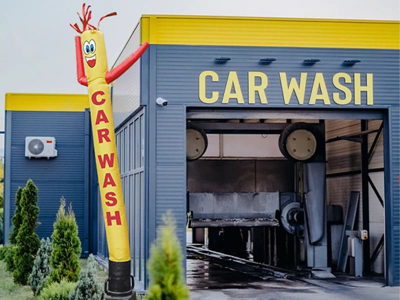 A yellow inflatable tube man printed with the words Car Wash beside a car wash building