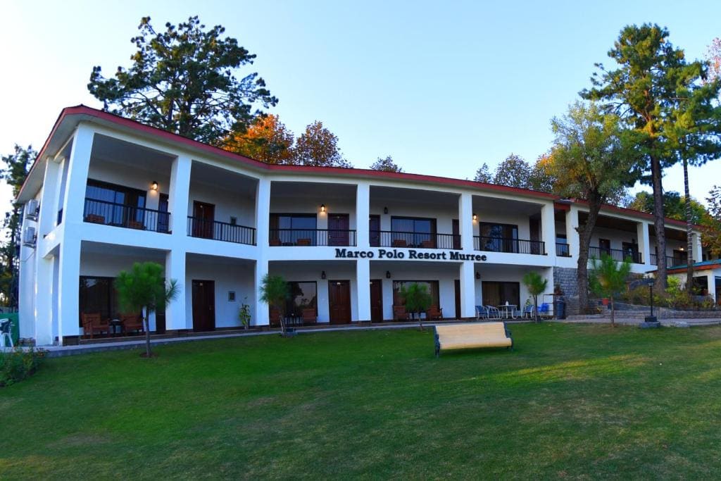 The white two-storey Marco Polo Resort Murree building with a lawn in front, under blue sky