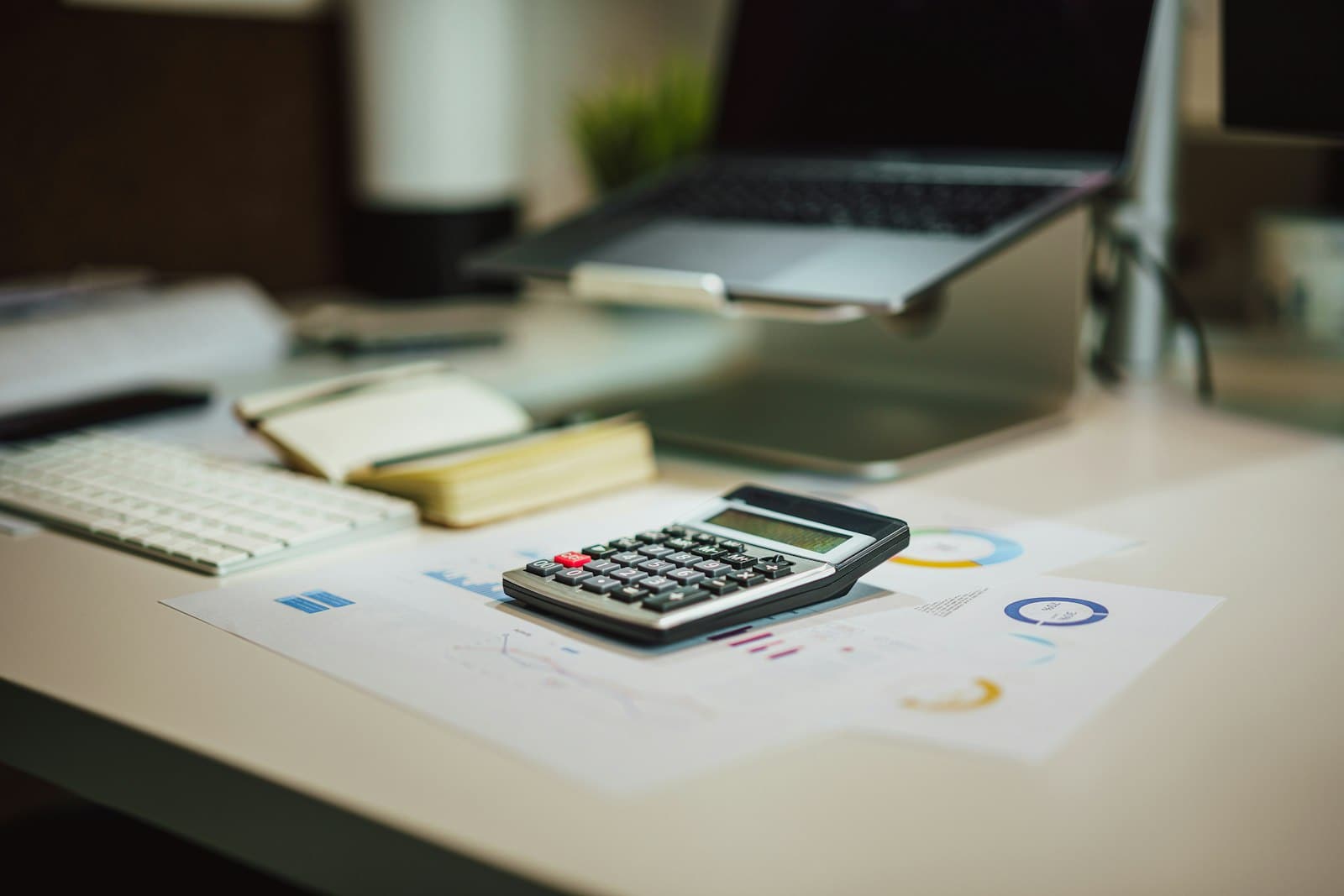 Calculator and printed financial reports on a desk beside a laptop on a stand